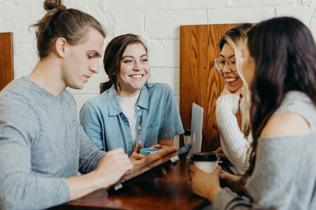 Four people sit around a wooden table with laptops and a tablet, collaborating.
